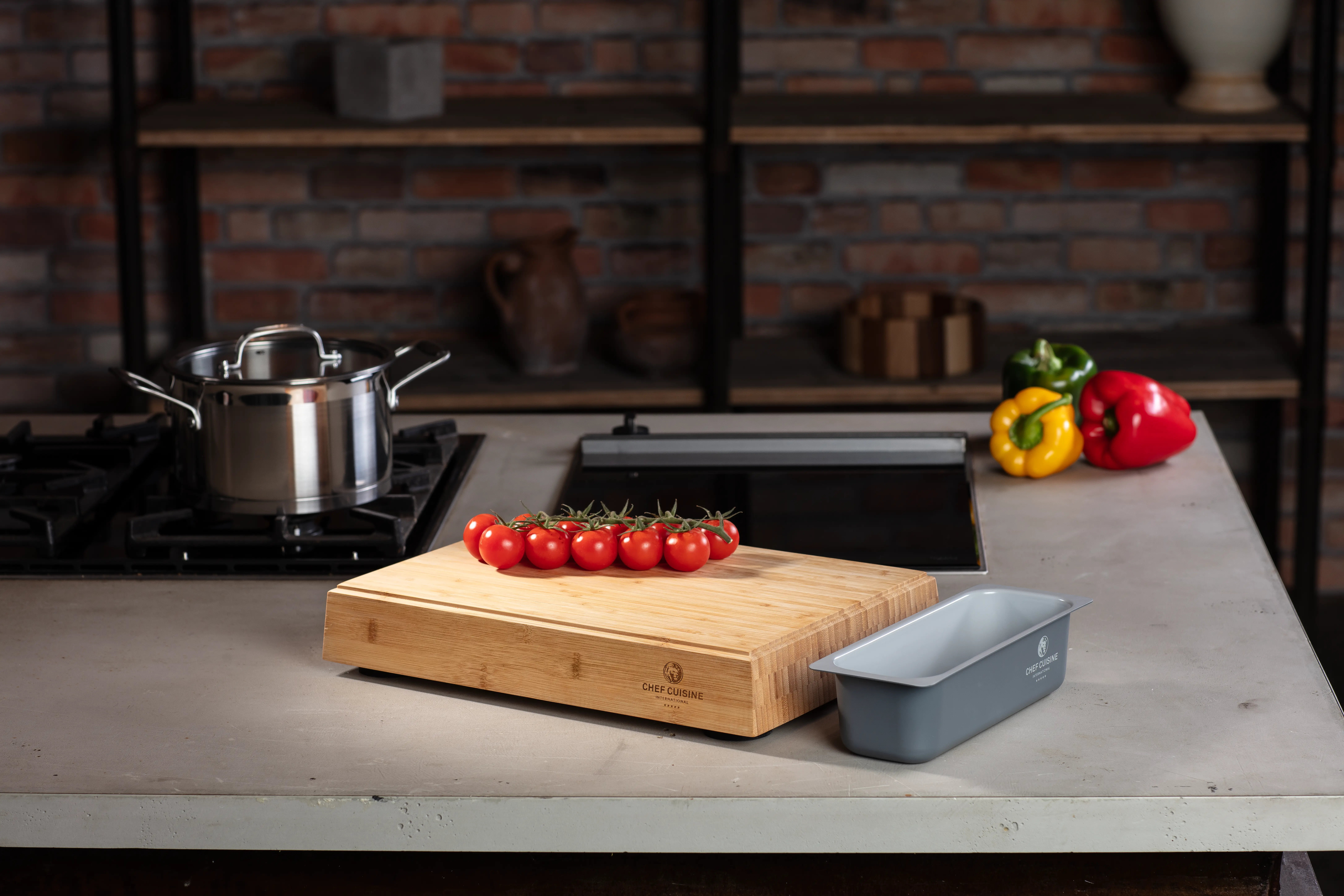 Magnetisches Bambus-Schneidebrett mit Food-Container und Tomaten auf Küchenarbeitsfläche, im Hintergrund Topf mit Paprika